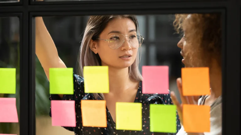 Professional team member brainstorming ideas with colourful Post-it notes on a glass wall.