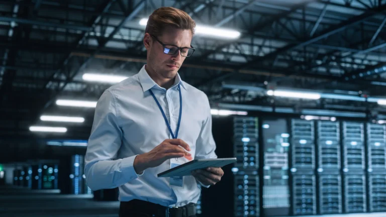 Professional analysing data on a tablet in a high-tech server room, symbolising secure and efficient infrastructure.