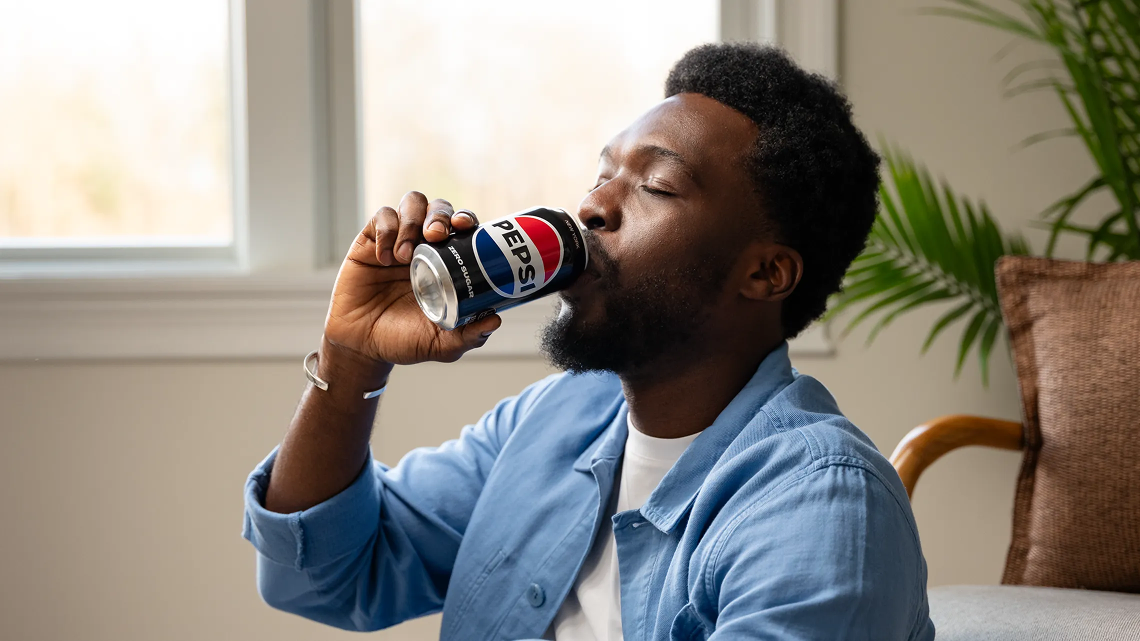 A man drinking Pepsi Zero Sugar from a can while seated in a relaxed environment.